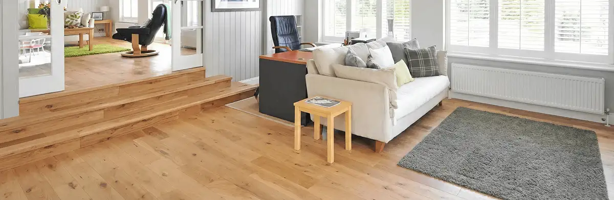 A modern living room with professionally installed laminate flooring, a beige sofa, a small side table, a gray rug, and large windows with white shutters in Cincinnati, OH